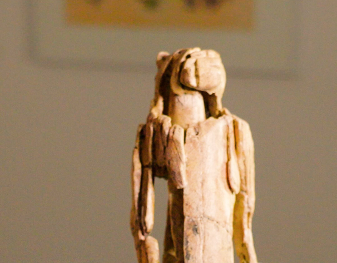 Nahaufnahme des Löwenmenschen, einer rund 40.000 Jahre alten Figur aus Mammutelfenbein, die in der Stadel-Höhle im Lonetal auf der Schwäbischen Alb entdeckt wurde. Die aufrecht stehende Figur vereint menschliche Körpermerkmale mit dem Kopf eines Höhlenlöwen. Eine Hand neben der Figur verdeutlicht ihre geringe Größe.